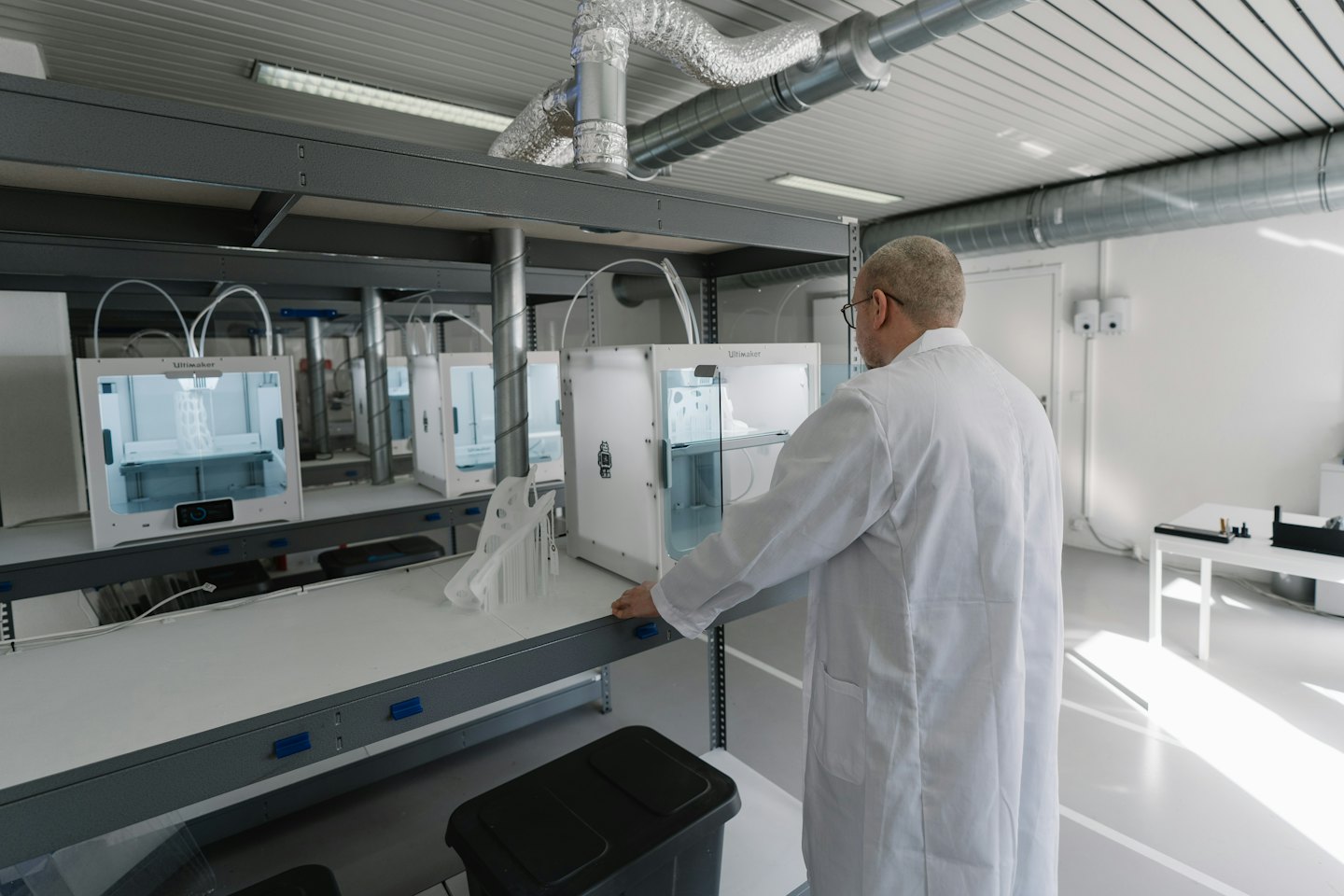 Man inspects 3D printer in a modern lab with multiple printers.